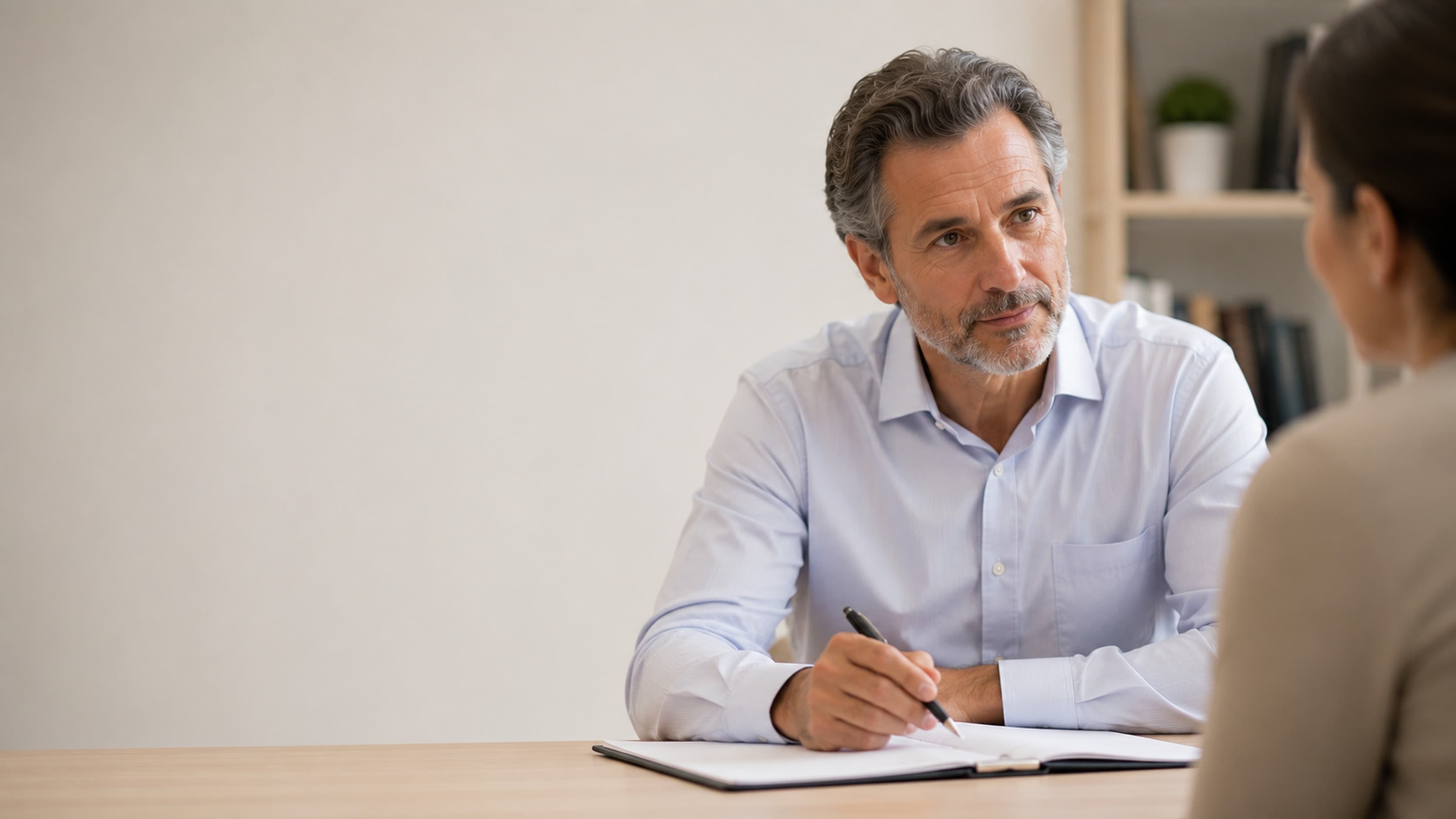 Psiquiatra da DoctorÁgape ouvindo com atenção uma paciente durante a consulta, com o caderno de anotações aberto sobre a mesa, no consultório, em Joinville